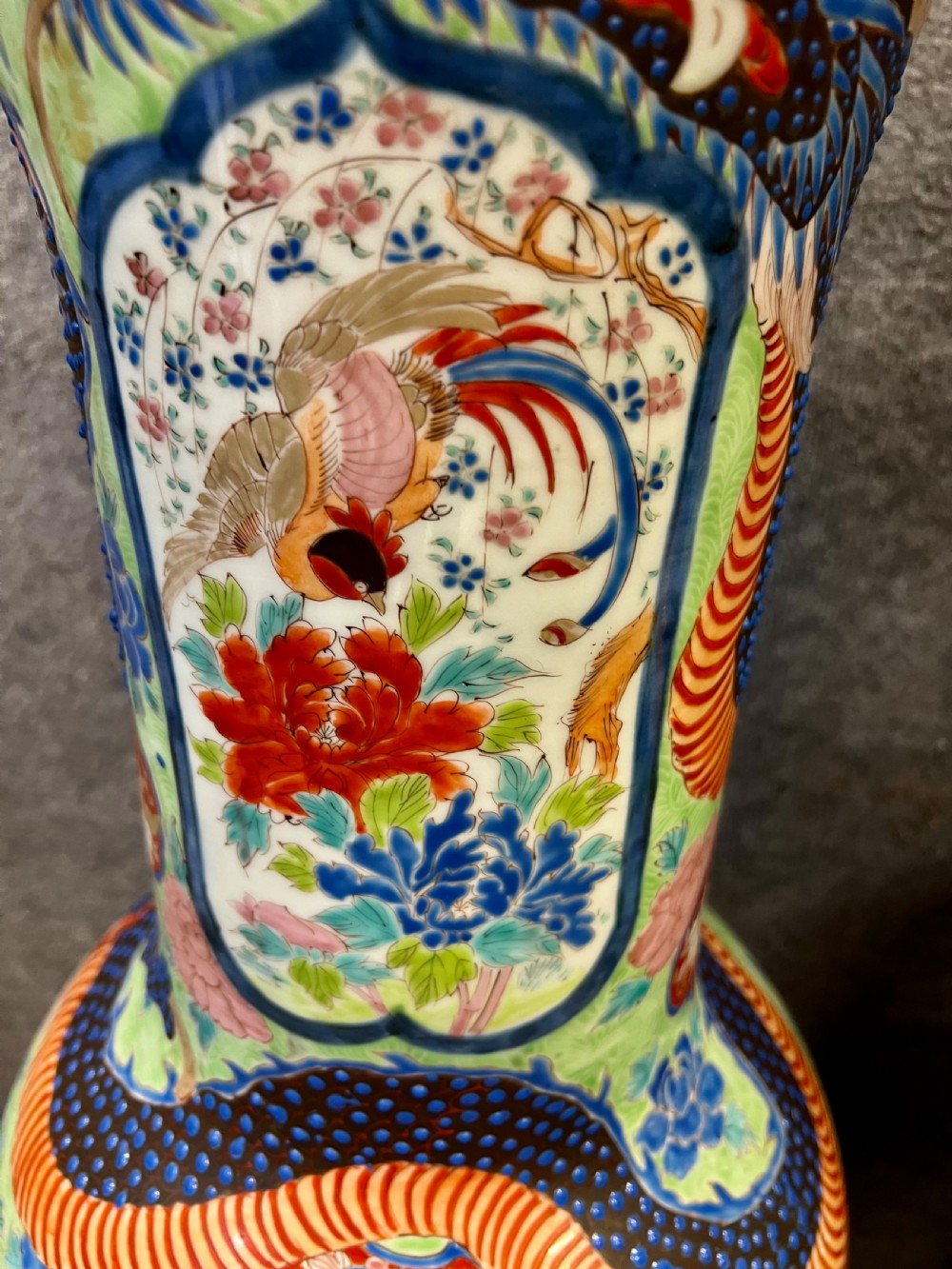 A pair of large, baluster-shaped Arita porcelain floor vases decorated with polychrome figures, floral motifs, and dragons, supported on carved dark wood bases. View X