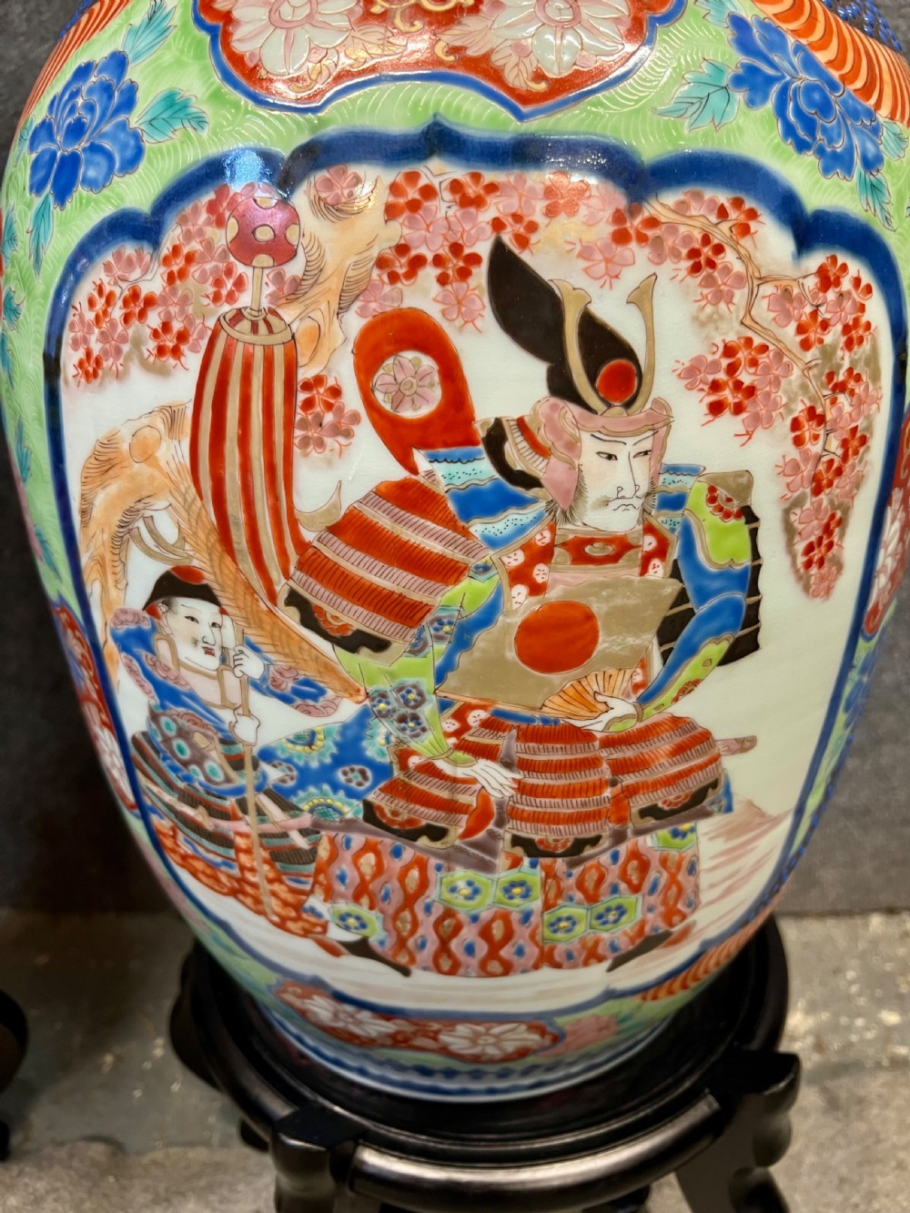 A pair of large, baluster-shaped Arita porcelain floor vases decorated with polychrome figures, floral motifs, and dragons, supported on carved dark wood bases. View XI
