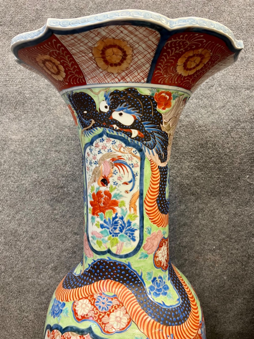 A pair of large, baluster-shaped Arita porcelain floor vases decorated with polychrome figures, floral motifs, and dragons, supported on carved dark wood bases. View XVI