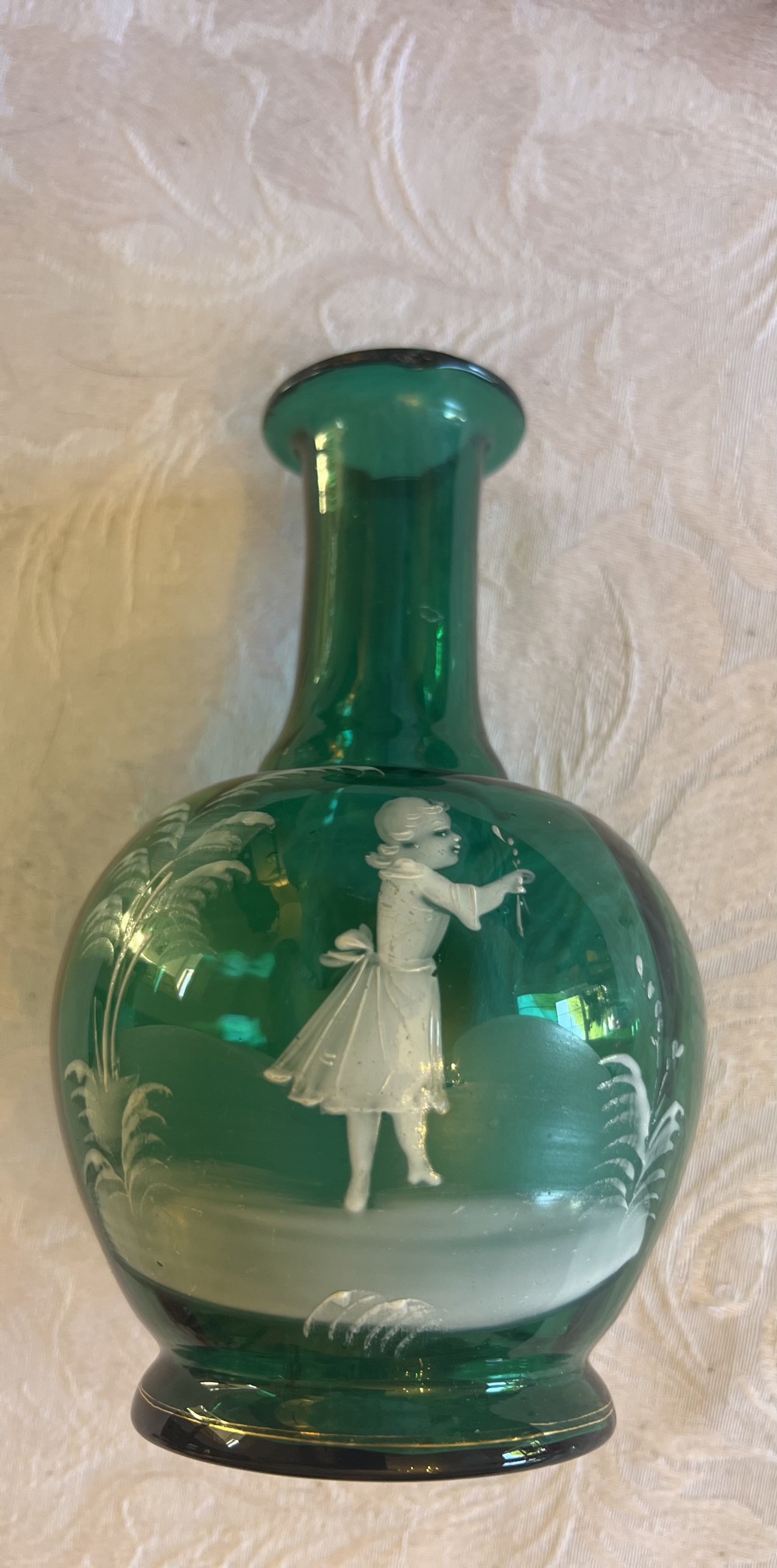 An emerald green glass vase featuring a white enamel painted scene of a child holding a plant sprig.