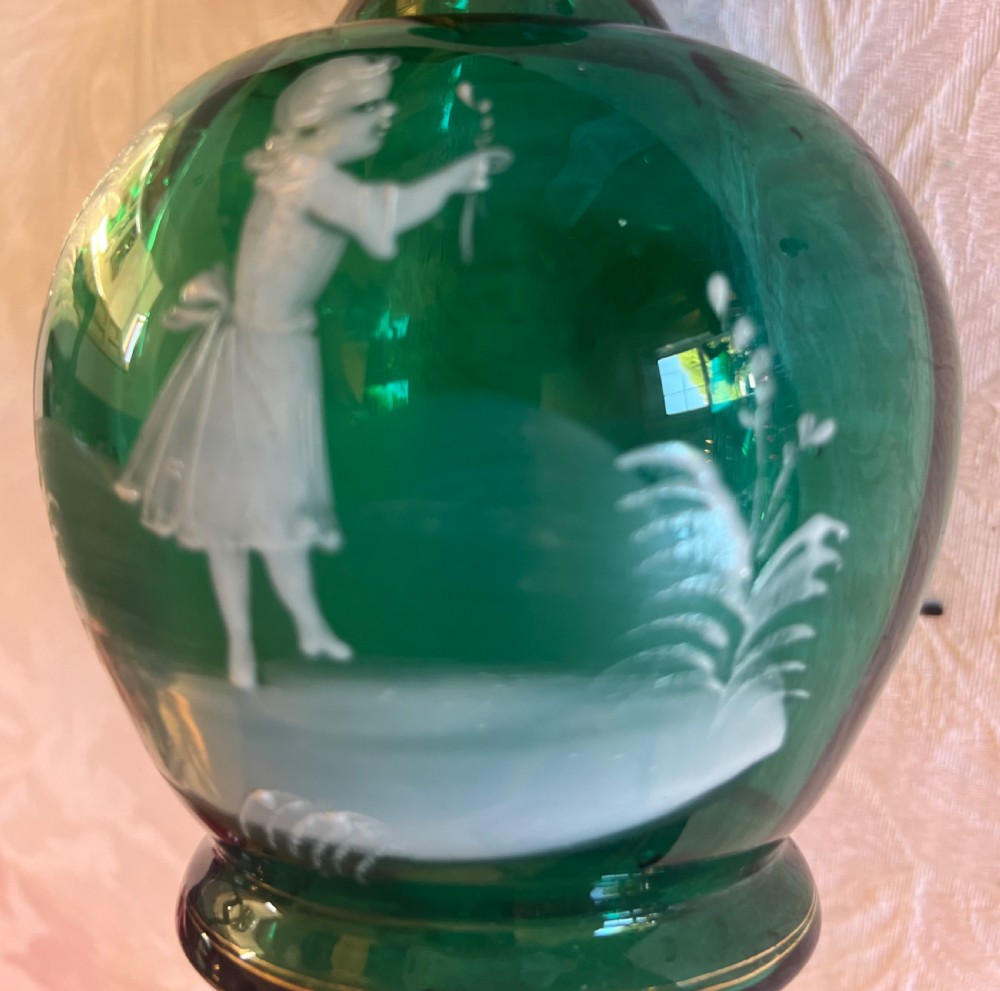 An emerald green glass vase featuring a white enamel painted scene of a child holding a plant sprig. View II