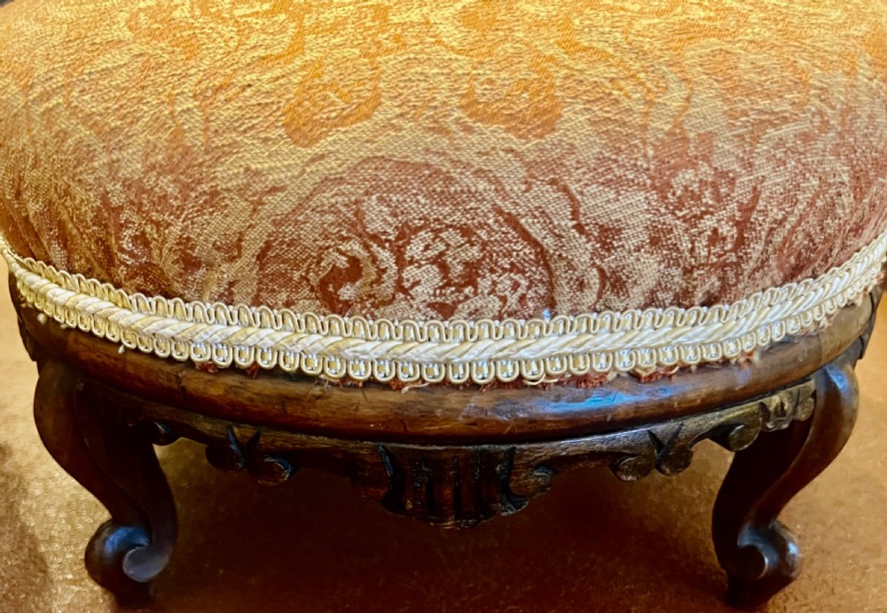 A matching pair of low circular Victorian footstools with patterned orange upholstery, decorative braid trim, and dark carved wooden legs. View III