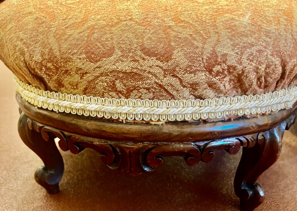 A matching pair of low circular Victorian footstools with patterned orange upholstery, decorative braid trim, and dark carved wooden legs. View IV