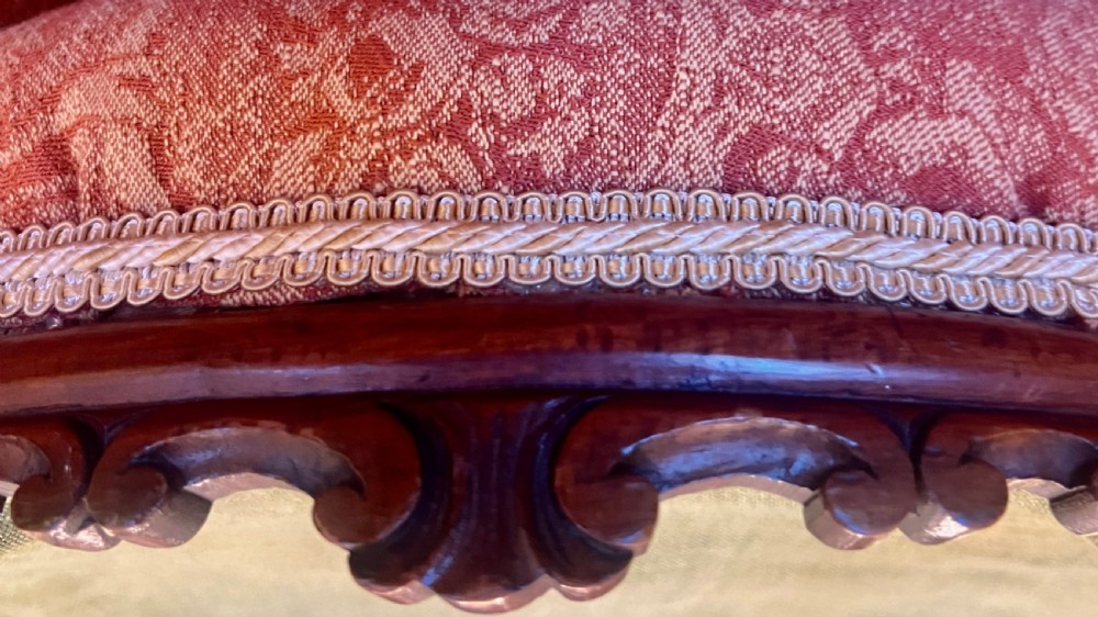 A matching pair of low circular Victorian footstools with patterned orange upholstery, decorative braid trim, and dark carved wooden legs. View V
