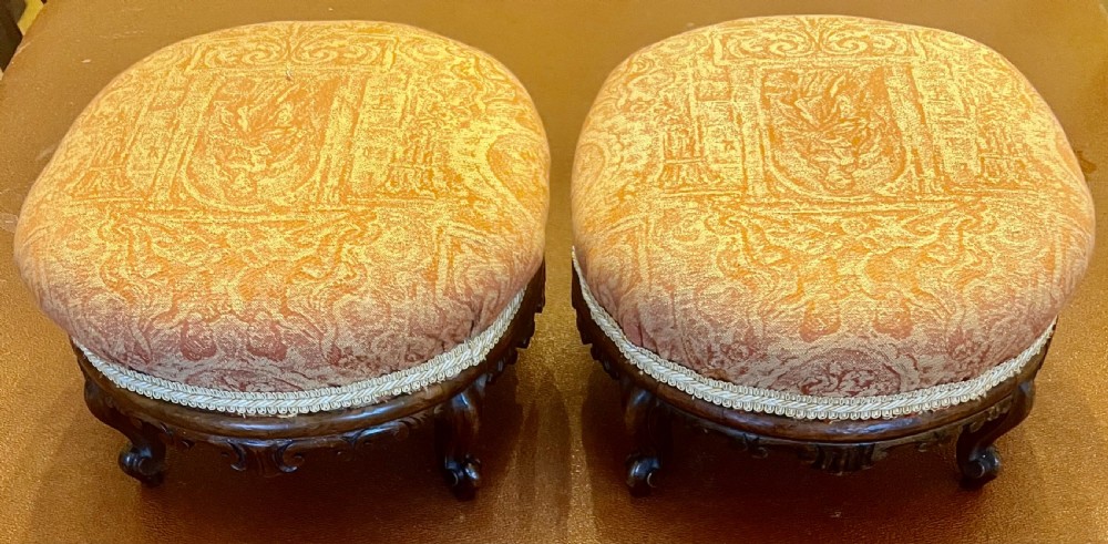 A matching pair of low circular Victorian footstools with patterned orange upholstery, decorative braid trim, and dark carved wooden legs. View IX