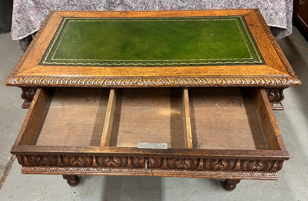 A 19th-century carved oak writing table featuring a green leather inset top, carved frieze, barley twist legs, and a central stretcher with finial. View IV
