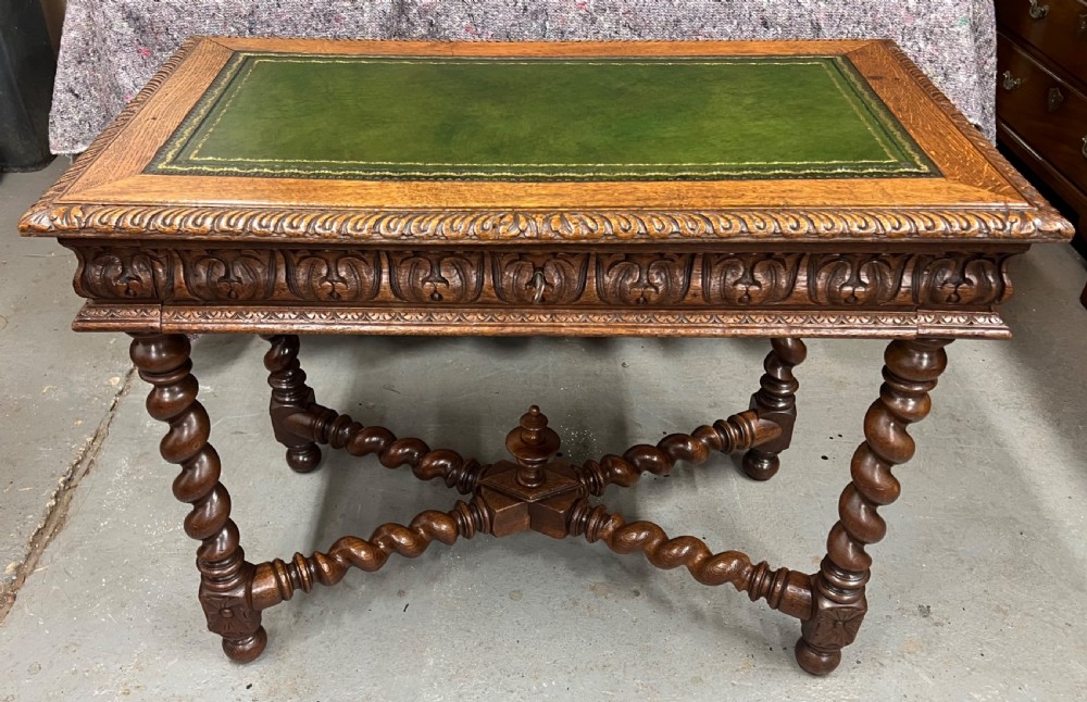 A 19th-century carved oak writing table featuring a green leather inset top, carved frieze, barley twist legs, and a central stretcher with finial. View V