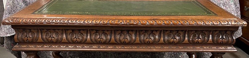 A 19th-century carved oak writing table featuring a green leather inset top, carved frieze, barley twist legs, and a central stretcher with finial. View VIII