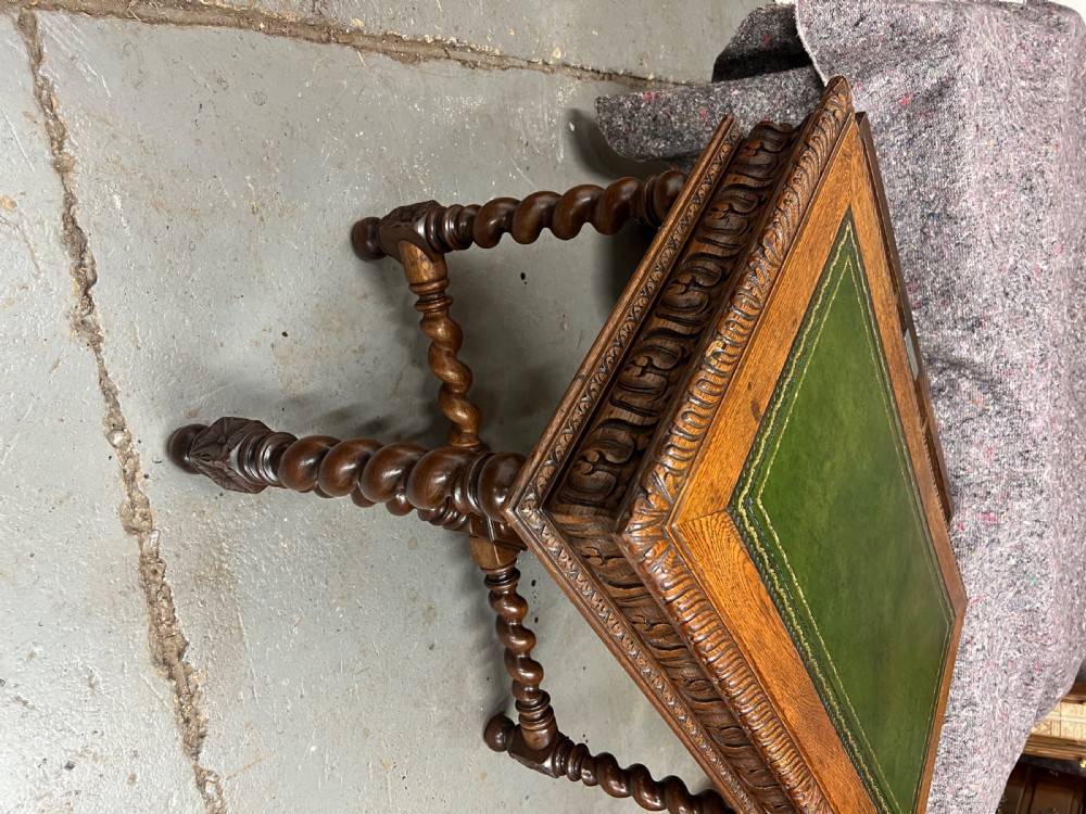 A 19th-century carved oak writing table featuring a green leather inset top, carved frieze, barley twist legs, and a central stretcher with finial. View X
