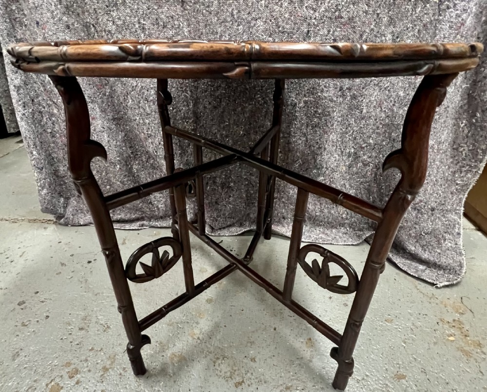 An oval brown hardwood coffee table with carved faux bamboo trim on a folding base. View II