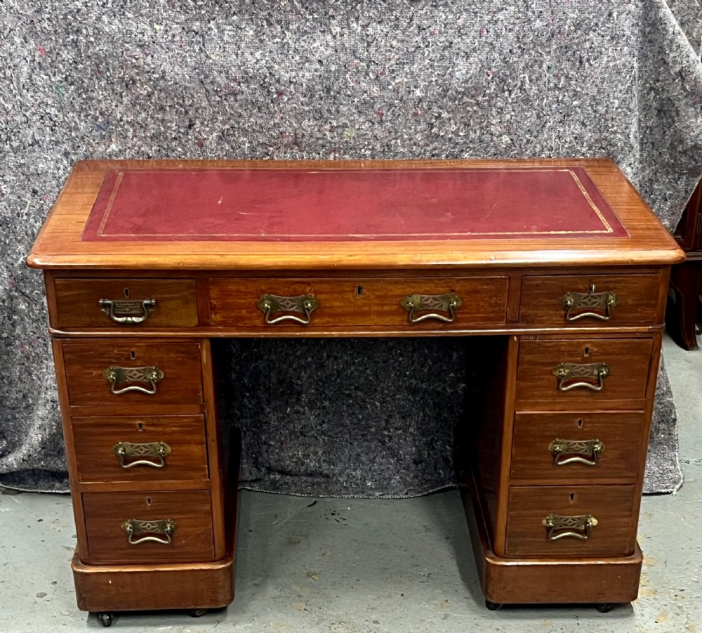 A compact Victorian mahogany pedestal desk featuring a red leather inset top, nine drawers with brass handles, and a plinth base on castors.