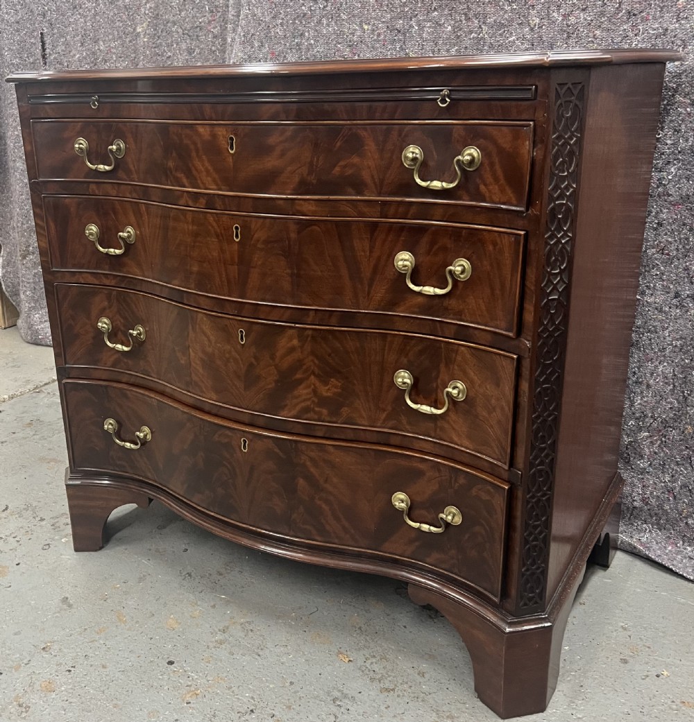 A Chippendale style mahogany chest of drawers featuring a serpentine front facade, carved blind fretwork canted corners, brass swan-neck handles, and bracket feet.