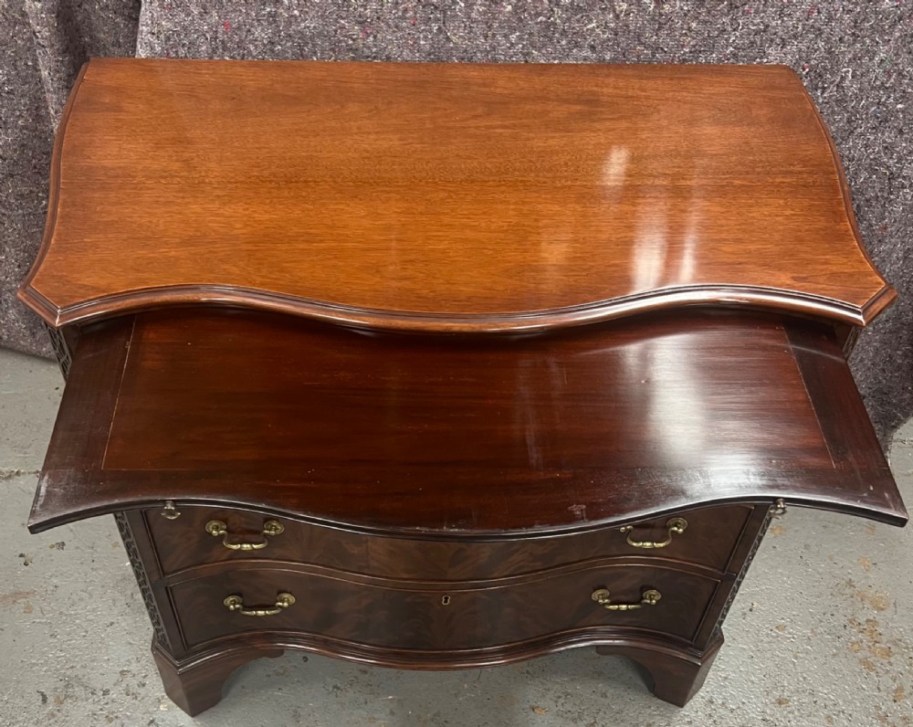 A Chippendale style mahogany chest of drawers featuring a serpentine front facade, carved blind fretwork canted corners, brass swan-neck handles, and bracket feet. View II