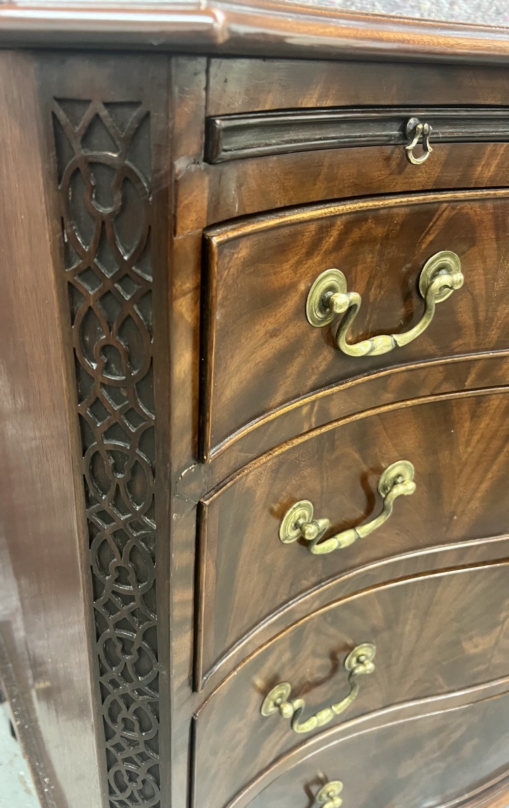 A Chippendale style mahogany chest of drawers featuring a serpentine front facade, carved blind fretwork canted corners, brass swan-neck handles, and bracket feet. View VII