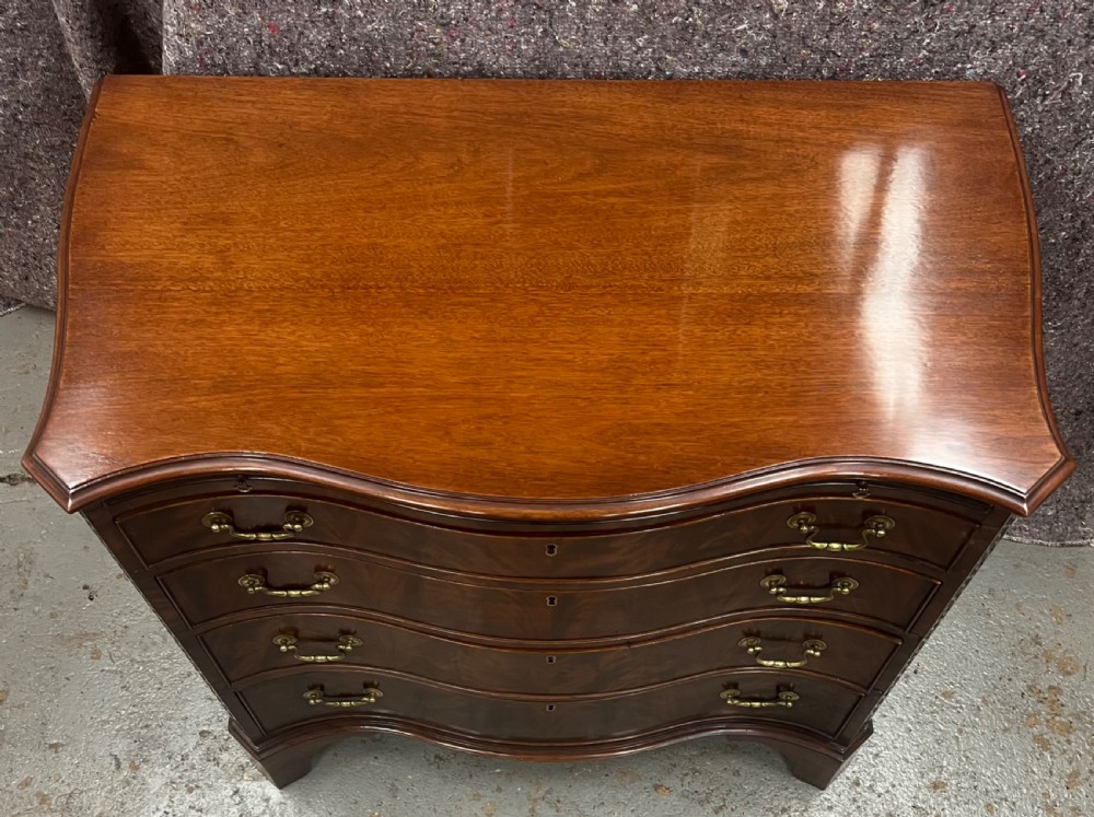 A Chippendale style mahogany chest of drawers featuring a serpentine front facade, carved blind fretwork canted corners, brass swan-neck handles, and bracket feet. View XI