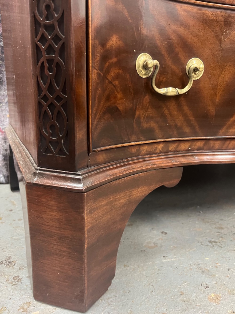 A Chippendale style mahogany chest of drawers featuring a serpentine front facade, carved blind fretwork canted corners, brass swan-neck handles, and bracket feet. View XII