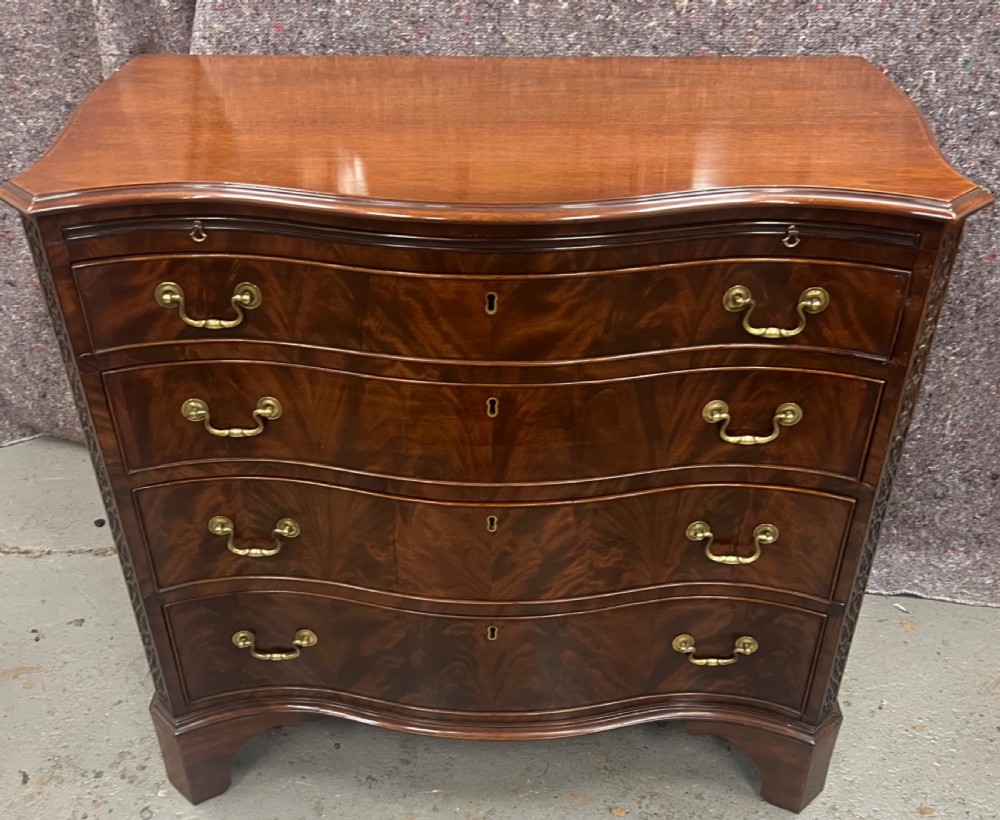 A Chippendale style mahogany chest of drawers featuring a serpentine front facade, carved blind fretwork canted corners, brass swan-neck handles, and bracket feet. View XIII