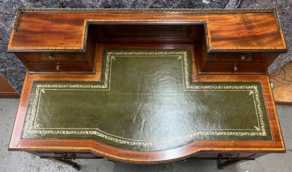 An Edwardian inlaid mahogany writing desk featuring a green leather inset writing surface, raised drawered superstructure, brass gallery top, and tapered square legs with castors. View II
