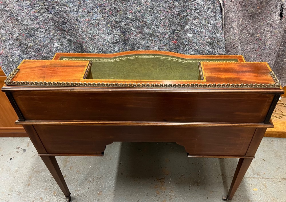 An Edwardian inlaid mahogany writing desk featuring a green leather inset writing surface, raised drawered superstructure, brass gallery top, and tapered square legs with castors. View IV