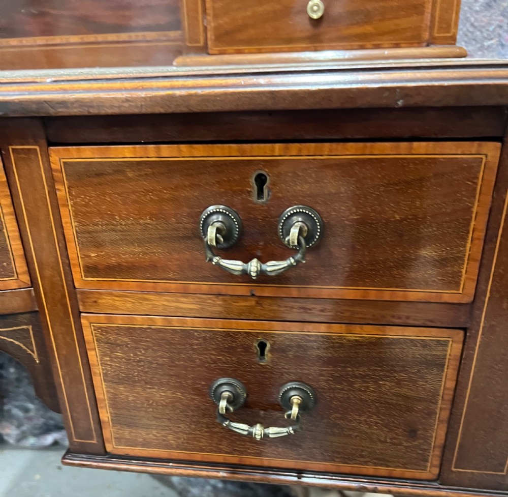 An Edwardian inlaid mahogany writing desk featuring a green leather inset writing surface, raised drawered superstructure, brass gallery top, and tapered square legs with castors. View XI