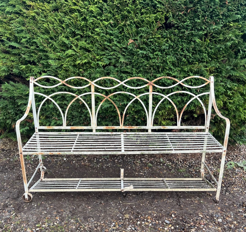 An off-white painted wrought iron garden seat featuring slatted strapwork construction, gothic backrest arches, and a lower footrest with weathered patina. View III