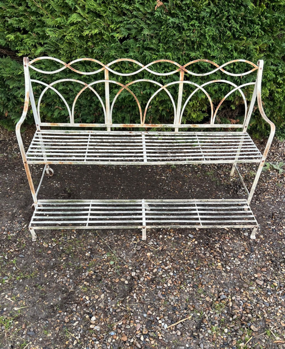 An off-white painted wrought iron garden seat featuring slatted strapwork construction, gothic backrest arches, and a lower footrest with weathered patina. View V