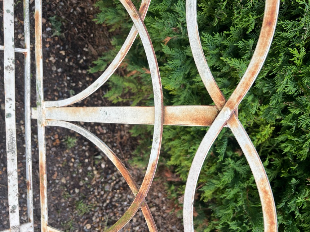 An off-white painted wrought iron garden seat featuring slatted strapwork construction, gothic backrest arches, and a lower footrest with weathered patina. View VI