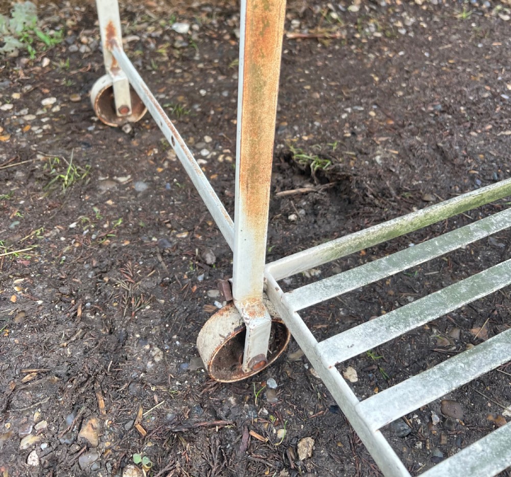 An off-white painted wrought iron garden seat featuring slatted strapwork construction, gothic backrest arches, and a lower footrest with weathered patina. View VII