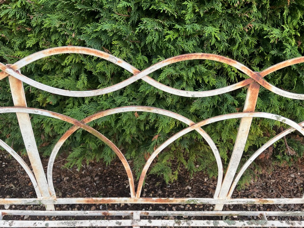 An off-white painted wrought iron garden seat featuring slatted strapwork construction, gothic backrest arches, and a lower footrest with weathered patina. View VIII