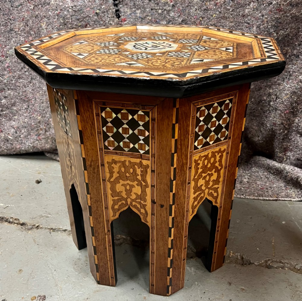An octagonal wooden side table decorated with intricate mother-of-pearl, bone, and marquetry geometric patterns and central Arabic calligraphy.