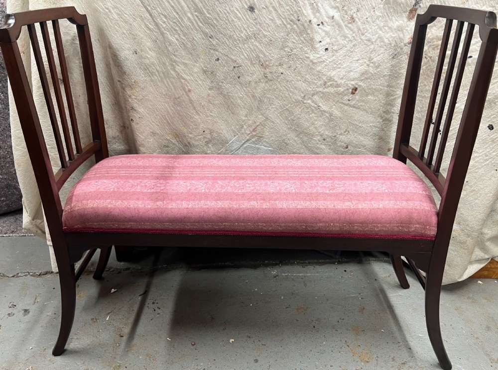An Edwardian mahogany window seat with slatted side armrests, curved legs, and a pink patterned upholstered cushion.