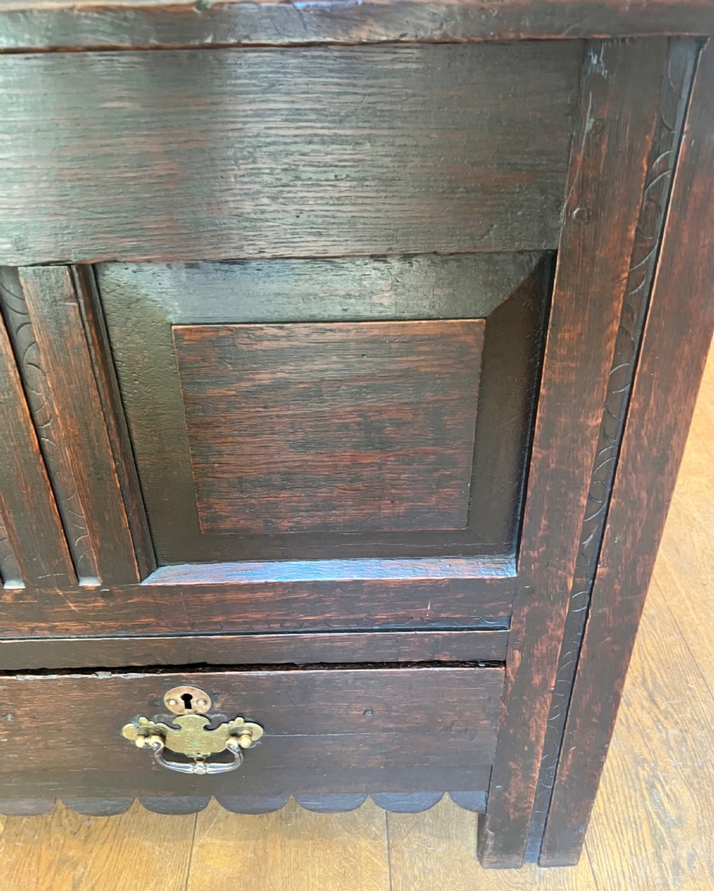 An eighteenth-century dark oak mule chest featuring a four-panel hinged lid, fielded panel front, and two lower drawers with brass drop handles. View IV