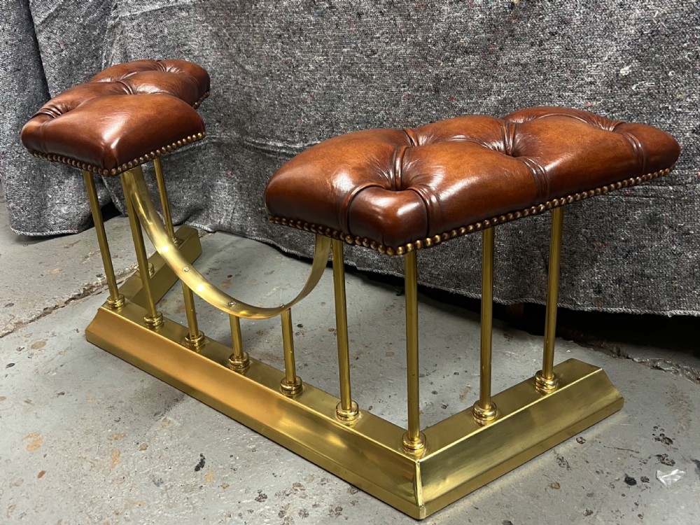 A brass fireplace club fender featuring two deep-buttoned brown leather seats supported by vertical brass spindles on a shaped metal base. View II