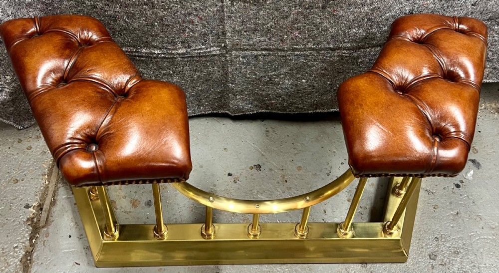 A brass fireplace club fender featuring two deep-buttoned brown leather seats supported by vertical brass spindles on a shaped metal base. View III