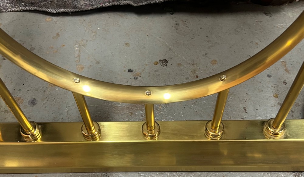 A brass fireplace club fender featuring two deep-buttoned brown leather seats supported by vertical brass spindles on a shaped metal base. View VII