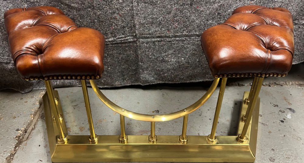A brass fireplace club fender featuring two deep-buttoned brown leather seats supported by vertical brass spindles on a shaped metal base. View VIII