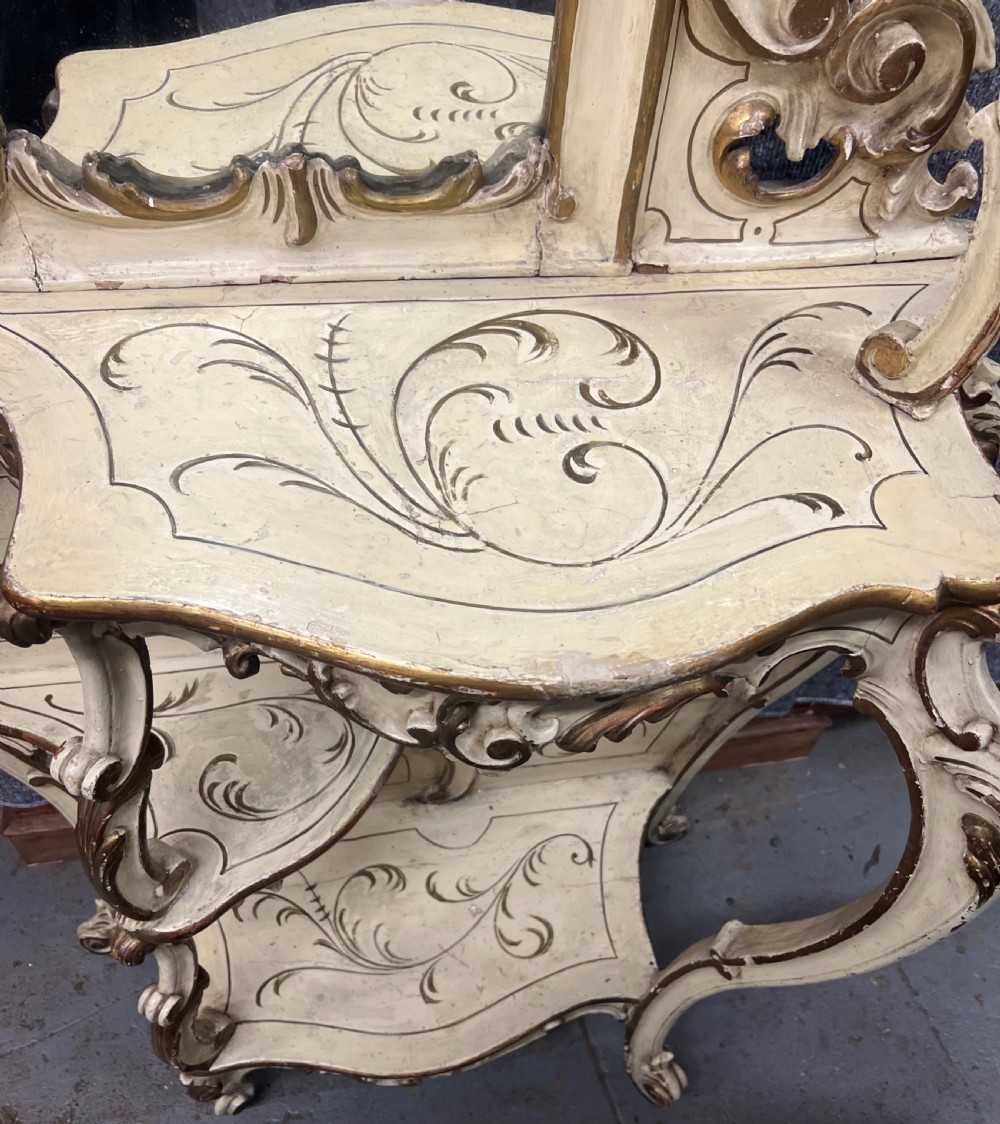 An ornate cream-painted and parcel-gilt Venetian Rococo console table featuring an asymmetrical tall mirror, tiered display shelves, and scrolling cabriole legs. View III