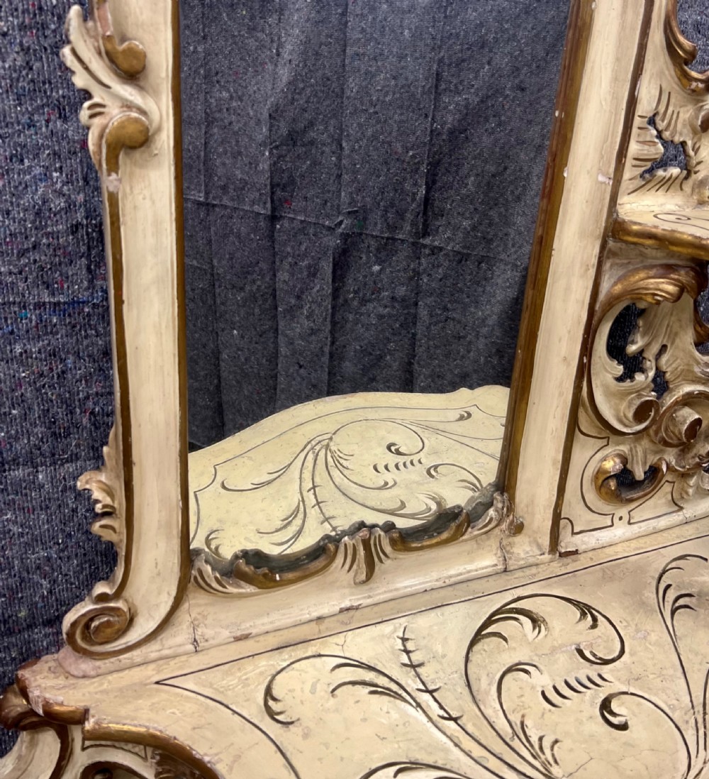 An ornate cream-painted and parcel-gilt Venetian Rococo console table featuring an asymmetrical tall mirror, tiered display shelves, and scrolling cabriole legs. View V