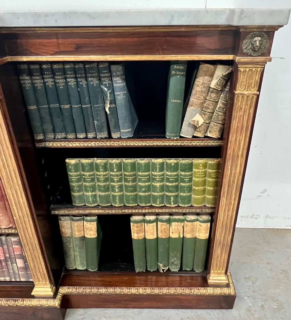 A low three-bay Regency style rosewood open bookcase with a white marble top, fluted gilded pilasters, and carved lion head mounts. View VI