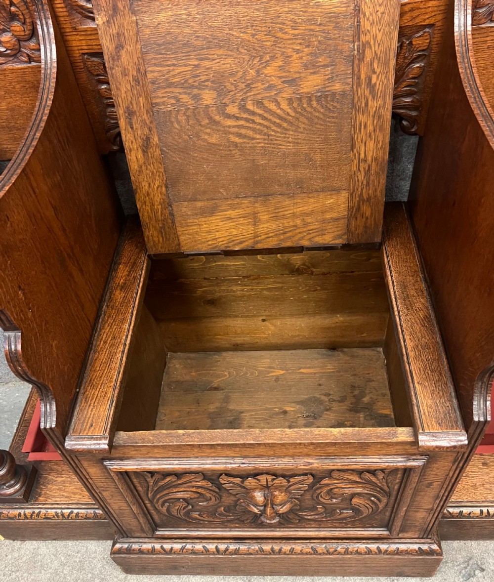 An antique carved oak hall stand set featuring a top wall-mounted mirror with coat pegs and a matching lower bench with integrated umbrella holders. View XIII