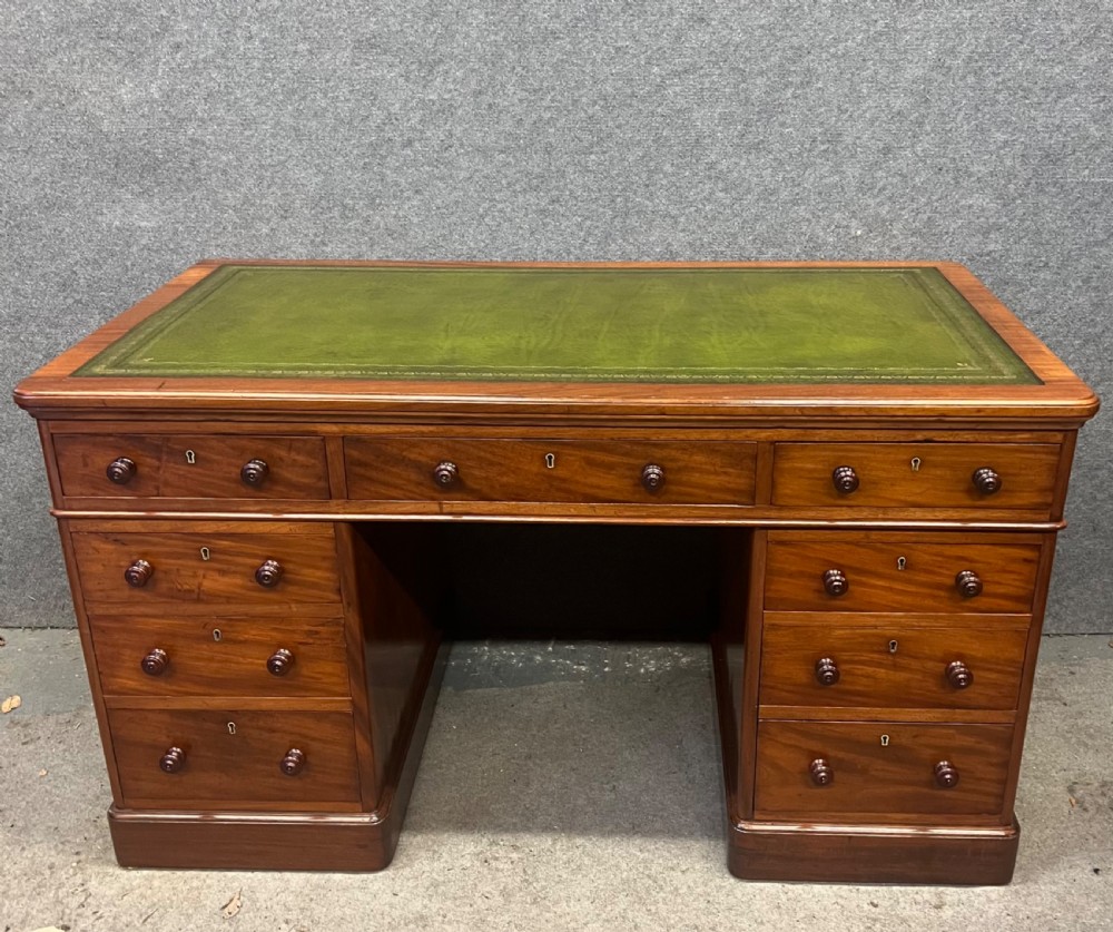 A nineteenth-century mahogany pedestal desk featuring a green leather writing top and nine drawers with turned wooden handles.