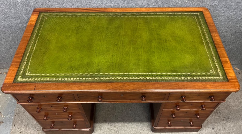 A nineteenth-century mahogany pedestal desk featuring a green leather writing top and nine drawers with turned wooden handles. View II