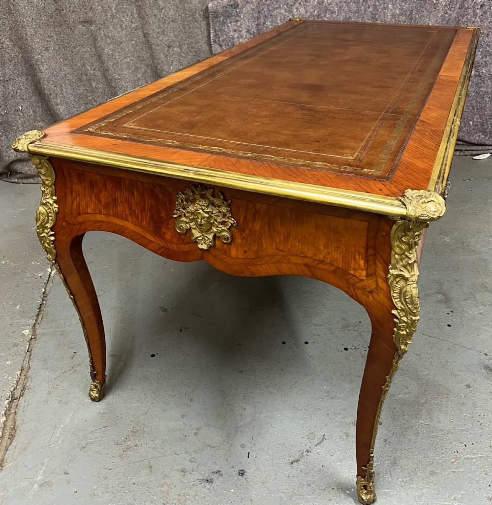 A nineteenth-century French bureau plat desk featuring wood marquetry, curved cabriole legs, ornate gilt-bronze mounts, three frieze drawers, and a leather inset writing top. View II