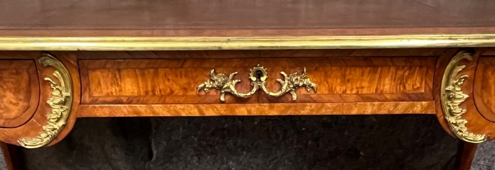 A nineteenth-century French bureau plat desk featuring wood marquetry, curved cabriole legs, ornate gilt-bronze mounts, three frieze drawers, and a leather inset writing top. View V