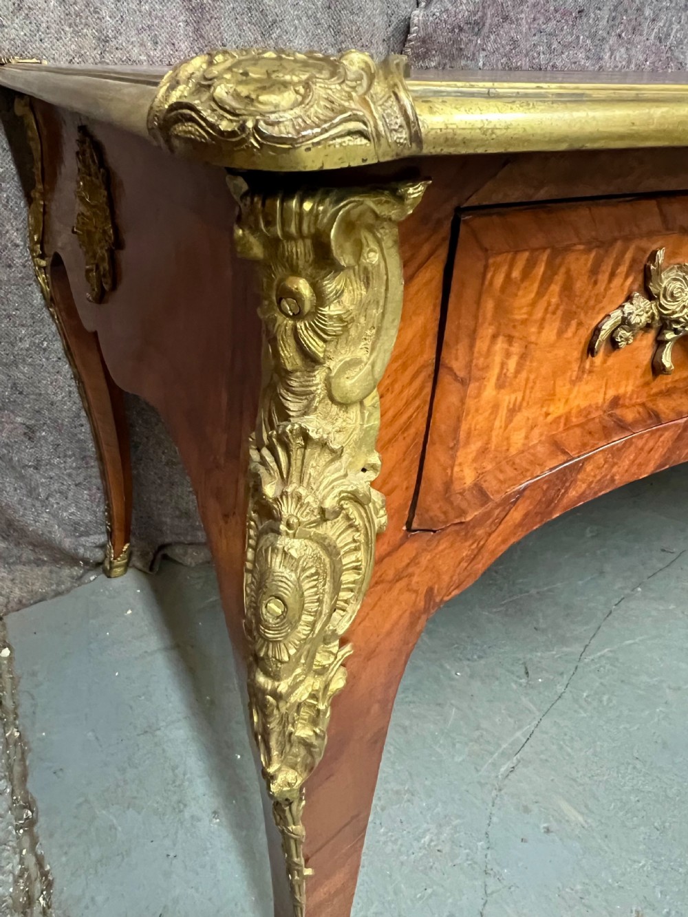A nineteenth-century French bureau plat desk featuring wood marquetry, curved cabriole legs, ornate gilt-bronze mounts, three frieze drawers, and a leather inset writing top. View VI