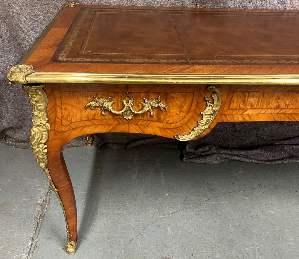A nineteenth-century French bureau plat desk featuring wood marquetry, curved cabriole legs, ornate gilt-bronze mounts, three frieze drawers, and a leather inset writing top. View VIII