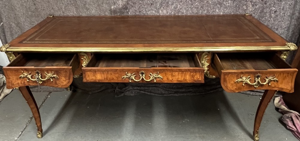 A nineteenth-century French bureau plat desk featuring wood marquetry, curved cabriole legs, ornate gilt-bronze mounts, three frieze drawers, and a leather inset writing top. View XII