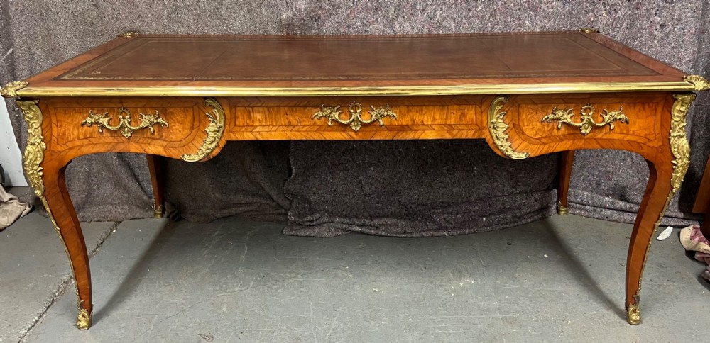 A nineteenth-century French bureau plat desk featuring wood marquetry, curved cabriole legs, ornate gilt-bronze mounts, three frieze drawers, and a leather inset writing top. View XIII