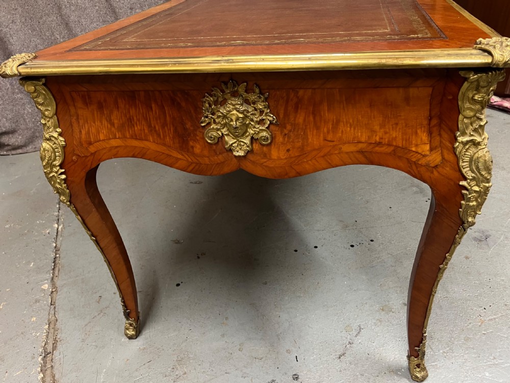 A nineteenth-century French bureau plat desk featuring wood marquetry, curved cabriole legs, ornate gilt-bronze mounts, three frieze drawers, and a leather inset writing top. View XIV