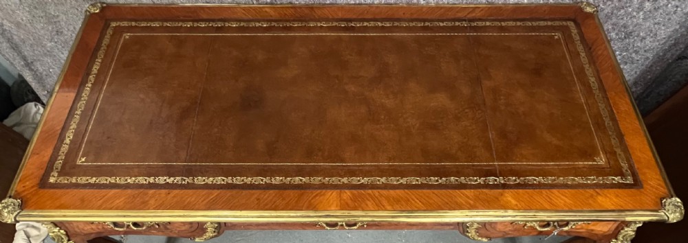 A nineteenth-century French bureau plat desk featuring wood marquetry, curved cabriole legs, ornate gilt-bronze mounts, three frieze drawers, and a leather inset writing top. View XV